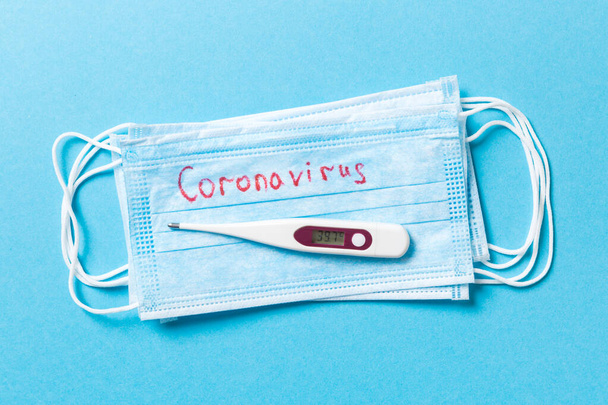 Draufsicht auf einen Haufen medizinischer Schutzmasken mit Coronavirus-Wort und einem Thermometer auf blauem Hintergrund. Atemwegssyndrom. Schützen Sie Ihr Gesundheitskonzept. - Foto, Bild