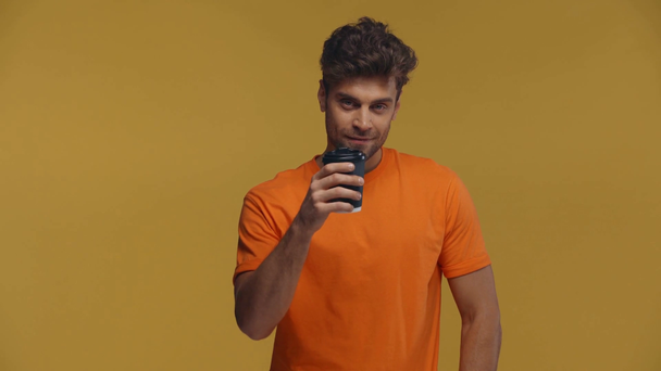 Man die koffie drinkt in papieren beker en kijkt naar camera geïsoleerd op geel - Video