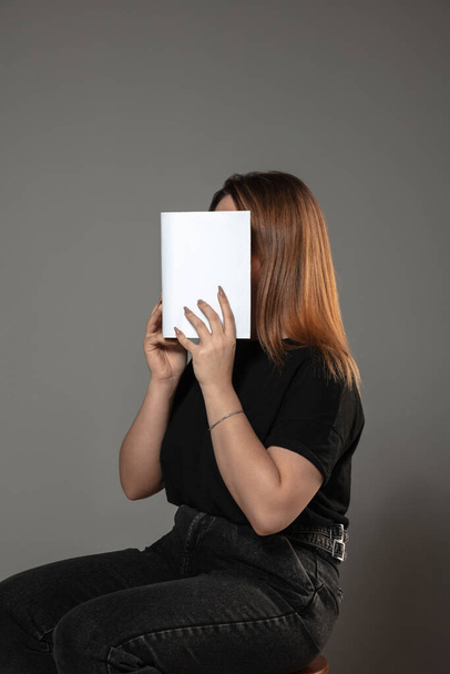 Happy world book day, read to become someone else - woman covering face with book while reading on grey background - Fotó, kép