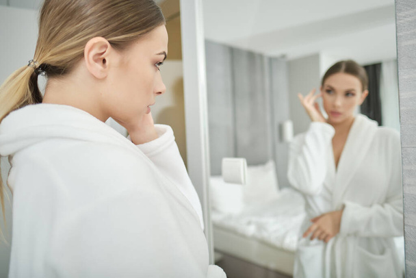 I am beautiful. Portrait of confident young woman looking at mirror with satisfaction while standing in bathrobe at home. Body care concept - Φωτογραφία, εικόνα