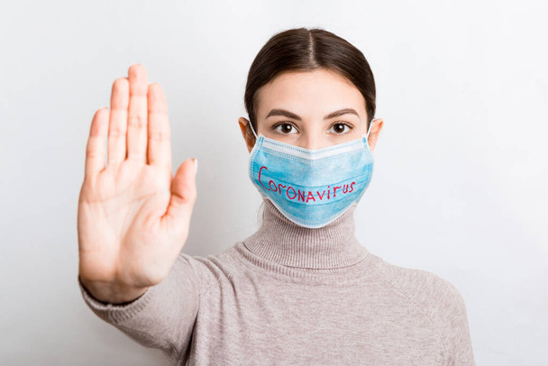 Retrato de una mujer con máscara médica con texto de coronavirus y gestos de stop en fondo blanco. Concepto de Coronavirus. Protección respiratoria
. - Foto, imagen