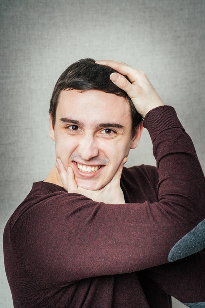 jonge man grimmig gezicht en houdt zijn hoofd met handen - Foto, afbeelding