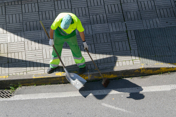 Zamiatarka uliczna z miotłą i łopatą pracująca nad miastem. Koncepcja czyszczenia publicznego - Zdjęcie, obraz