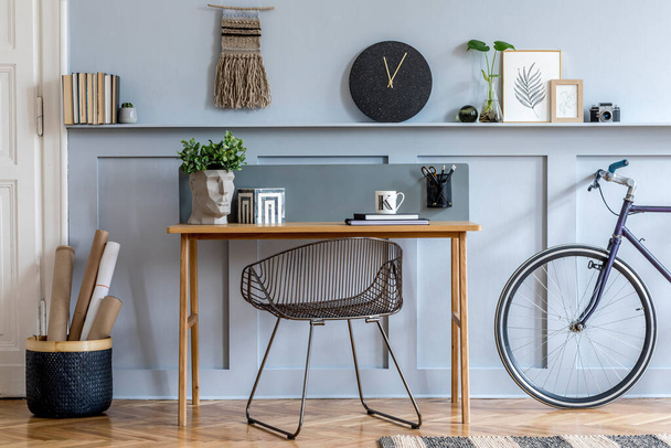 Diseño interior escandinavo de espacio abierto con escritorio de madera, silla moderna, paneles de madera con estante, planta, alfombra, bicicleta, suministros de oficina y elegantes accesorios personales
. - Foto, imagen