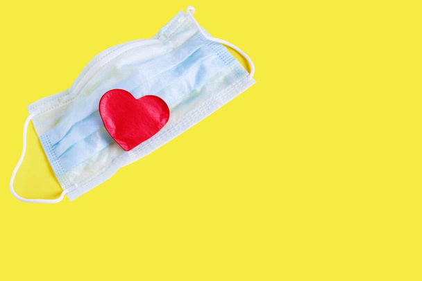 Medical protective face mask and red heart on yellow. ?aring for others . Healthcare and medical concept. Protection from coronavirus covid-2019 - Valokuva, kuva