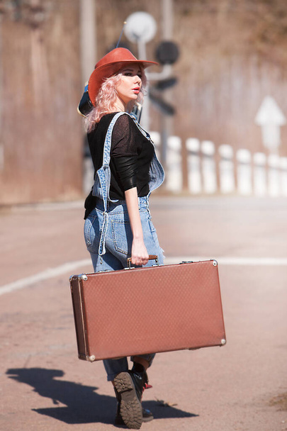 Nuori matkustava nainen matkalaukku liftaaminen tiellä
 - Valokuva, kuva
