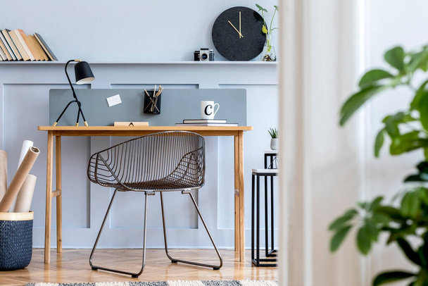 Scandinavian home office interior with wooden desk, design chair, wood panleing with shelf, plant, black clock, table lamp, office supplies and elegant accessories in modern home decor. - Photo, image