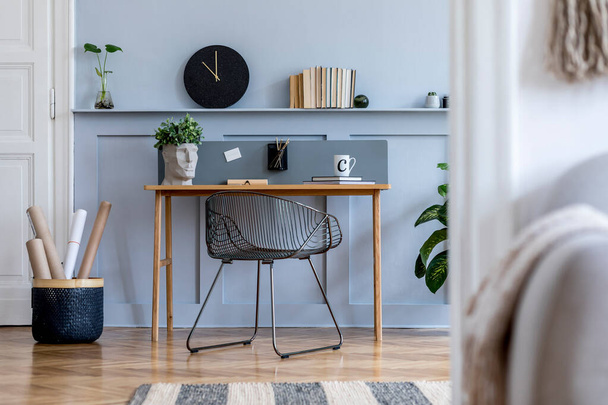 Scandinavian home office interior with wooden desk, design chair, wood panleing with shelf, plant, black clock, office supplies and elegant accessories in modern home decor. - Photo, image