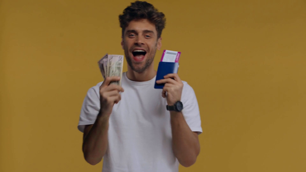 Χαμογελώντας άνθρωπος που κατέχει χρήματα, διαβατήριο και αεροπορικό εισιτήριο απομονώνονται σε κίτρινο - Πλάνα, βίντεο