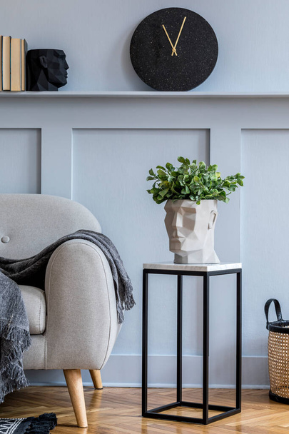 Elegante interior escandinavo da sala de estar com sofá cinza, xadrez, relógio preto, painéis de madeira com prateleira, tamborete de mármore, plantas e acessórios pessoais elegantes na decoração da casa de design
.  - Foto, Imagem