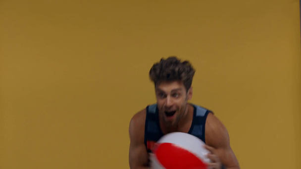 Hombre alegre lanzando bola inflable aislado en amarillo
 - Metraje, vídeo