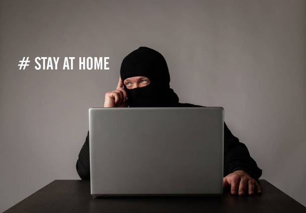 テロリストは、 COVID-19コロナウイルス発生の間、自宅に滞在しています。隔離の概念。ネットを閲覧するためにラップトップを使用してマスクの男. - 写真・画像