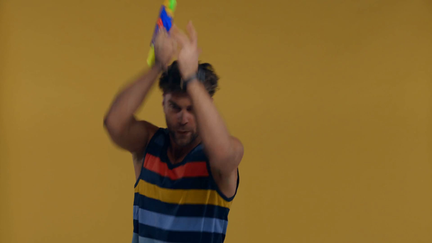 Bonito homem brincando com arma de brinquedo isolado no amarelo
 - Filmagem, Vídeo