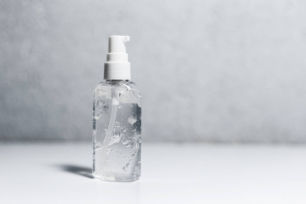 Close-up of portable plastic bottle with sanitizer antiseptic gel on white table. Background of grey textured wall. - Фото, зображення