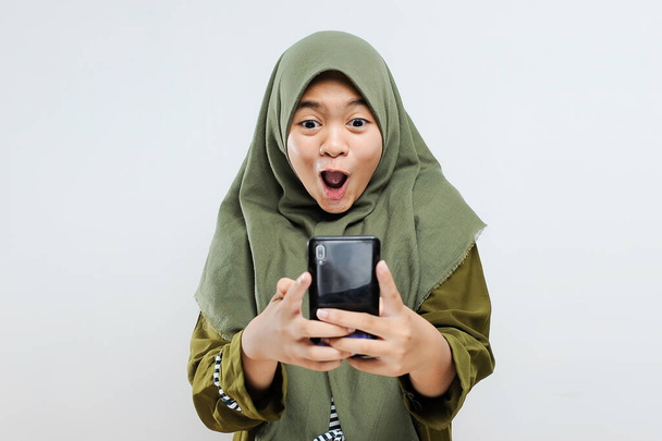 Jeune asiatique excitée femme musulmane choc regarder smartphone obtenir le meilleur cadeau / bon / discount, isolé sur gris
 - Photo, image
