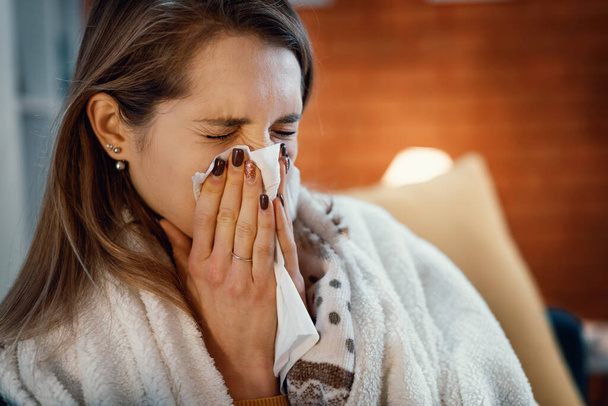 Young woman covering herself with a blanket and blowing her nose, she has cold and flu - Foto, afbeelding