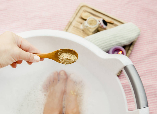 Egy nő, aki gyógyító lábfürdőt vesz mustárporral, mustárport ad a lábfürdőhöz fakanállal. Hideg betegség ellen fáj és javítja a vérkeringést. Alternatív gyógyászat.  - Fotó, kép