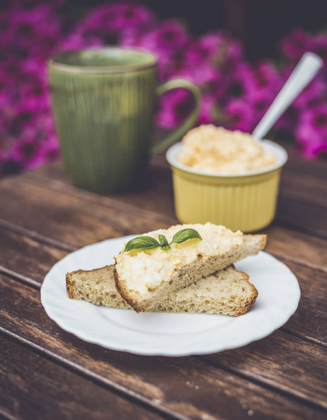 Délicieuse pâte jaune d'oeuf et de mayonnaise sur pain de blé entier, recette de collation pour le petit déjeuner, fleurs roses sur le fond, base en bois
. - Photo, image