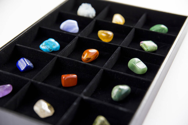 Разнообразие красочных полудрагоценных камней кристаллов в ящике организатора сортируется по цвету, выделенному на черном
. - Фото, изображение