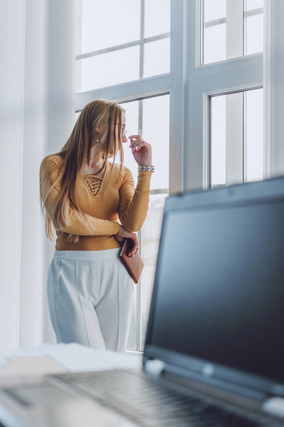 Smart working, agile, remotely working, Flexible hours, rearranged offices, new way of organising work. Employees have opportunity to work from home. Young woman stands at window in her home on laptop - Photo, image