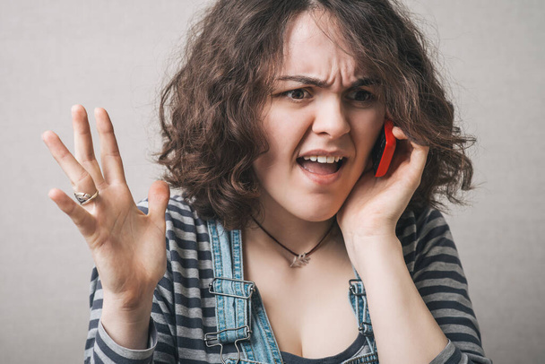 Woman talking on a cell phone, bad news surprised. Gray background - Φωτογραφία, εικόνα