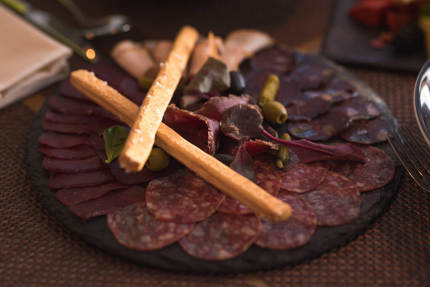 meat appetizer on a black plate with sausage, different types of meat, olives and crackers - Valokuva, kuva