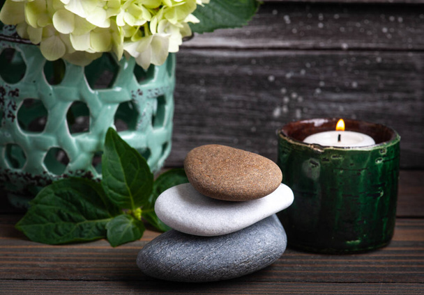 Green aroma candle in Spa still life on dark wooden background with hortensia flowers and pile of pebbles - Photo, Image