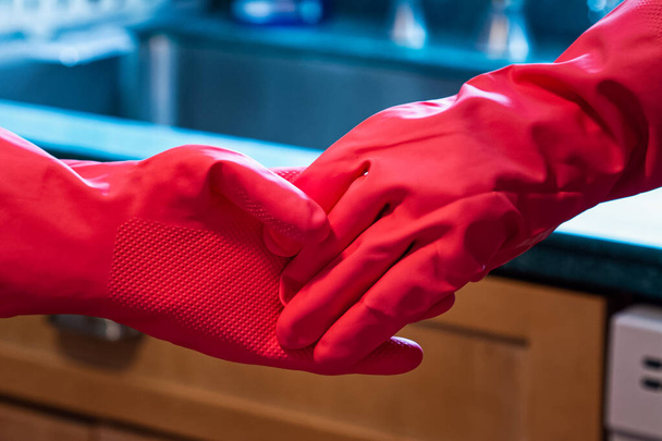 2人でキッチンで明るい色のラテックス手袋の手を保持します。病気と健康の間の家の中の社会的距離や消毒のプロセスを扱う人々を示しています。. - 写真・画像