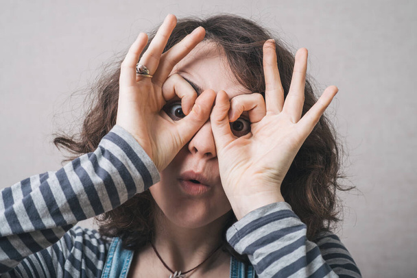 Young happy woman holding her hands over her eyes as glasses and  looking through fingers - Fotografie, Obrázek