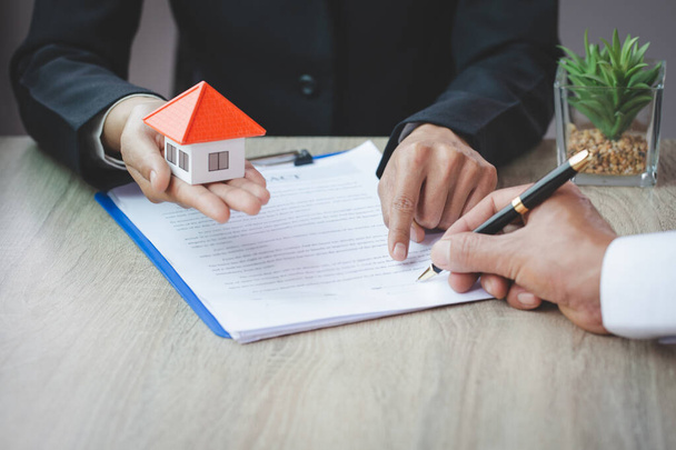 Una mujer firma un contrato para comprar una casa con un agente de bienes raíces. Modelo de casa en mano
. - Foto, Imagen