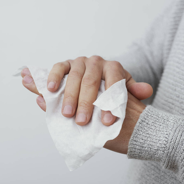 primer plano de un hombre caucásico, con un suéter gris pálido casual, desinfectando sus manos con una toallita húmeda
 - Foto, imagen