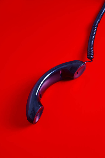 closeup of the handset of a black telephone in a red background - Foto, imagen