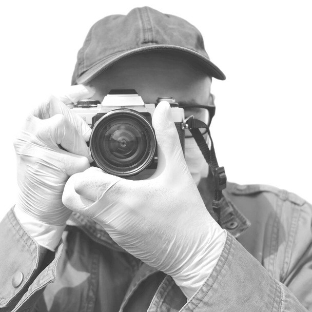 Fotograf w sterylnych rękawiczkach ochronnych trzymający kamerę 35 mm. Fotograf w czerni i bieli. - Zdjęcie, obraz