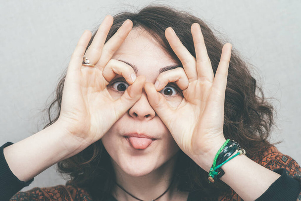 Girl teasing, showing tongue makes the binoculars hands - Foto, Bild