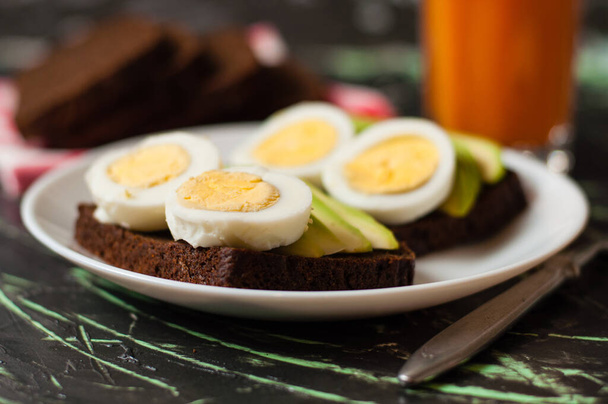 Μαύρο ψωμί ολικής αλέσεως, σάντουιτς με αυγά και αβοκάντο, χυμός πολλών φρούτων σε ψηλό ποτήρι. Έννοια σωστή διατροφή, πρωινό. - Φωτογραφία, εικόνα