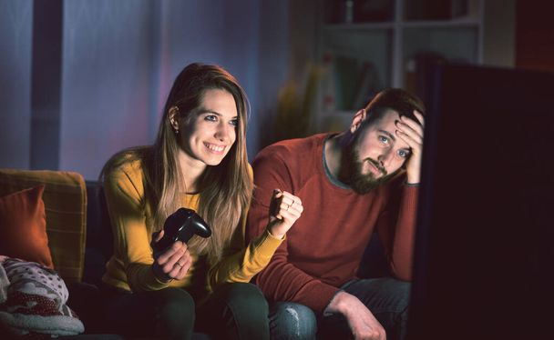 Happy couple playing video games at home, the girl won and is celebrating with fist raised - Fotó, kép