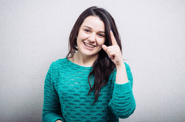 Woman with an index finger upward. On a gray background. - Fotografie, Obrázek