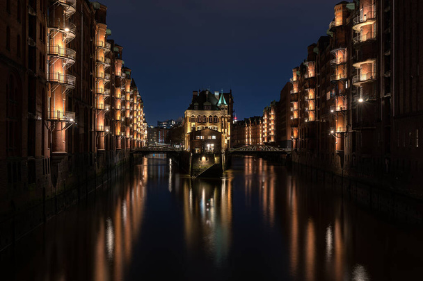 Het pakhuisdistrict Speicherstadt bij zonsondergang in Hamburg, Duitsland. Verlichte magazijnen in de wijk Hafencity in Hamburg. - Foto, afbeelding
