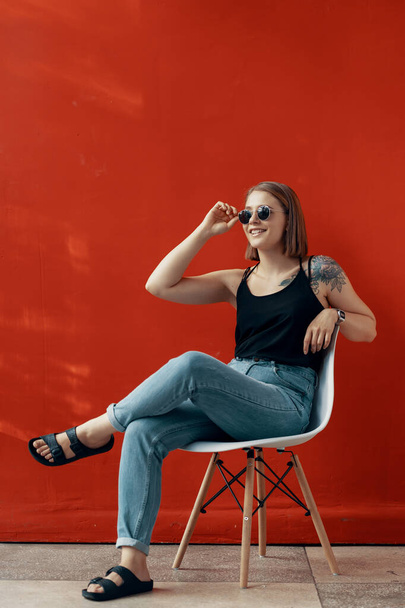 Menina sentada em uma cadeira branca perto da parede vermelha. Luz natural da janela
 - Foto, Imagem