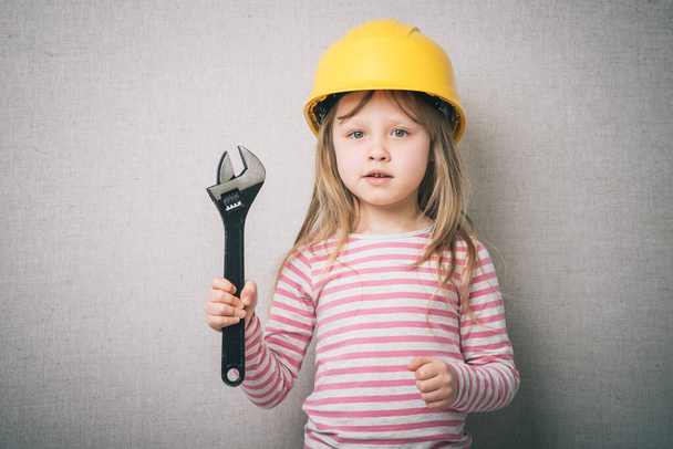 beautiful little girl in helmet with wrench isolated on gray background - Foto, imagen