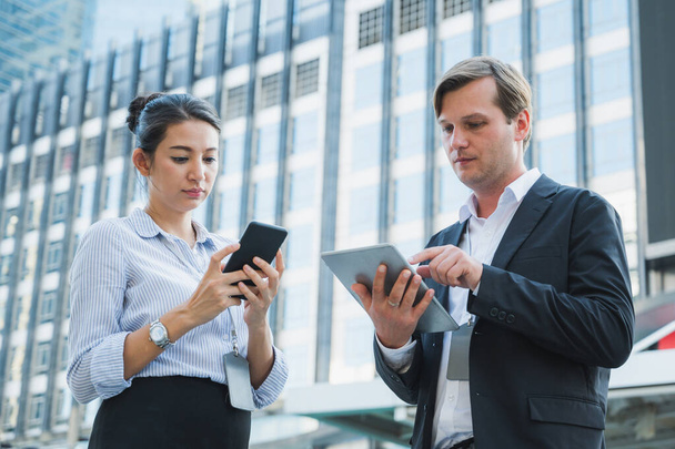 Portrait of businessman and woman using tablet and smartphone while standing on urban city background - Photo, image
