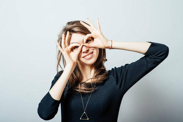 Young happy woman holding her hands over her eyes as glasses and  looking through fingers - Фото, изображение