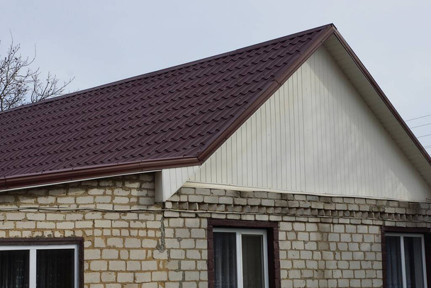 bílý soukromý cihlový dům s hnědou kachlovou střechou proti šedé obloze - Fotografie, Obrázek