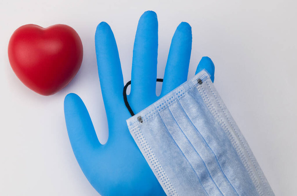 Lékařská maska a rukavice na bílém pozadí. Hračkové srdce. Koncept ochrany koronaviru - Fotografie, Obrázek