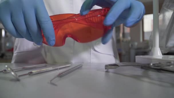 Close-up of dental equipment and protective eyeglasses lying on the table as young Caucasian woman coming up. Unrecognizable female stomatologist in gloves preparing for patient visit. Medicine. - Filmagem, Vídeo