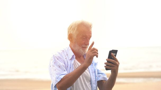 Lachende senior sms 'en via mobiele telefoon op het strand - Foto, afbeelding