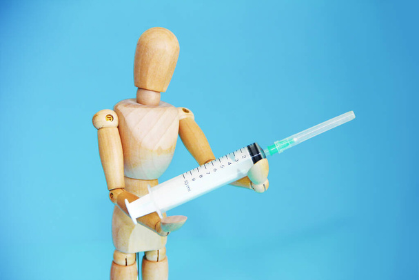 dřevěná žlutá figurína drží lékařskou stříkačku s lékem - Fotografie, Obrázek