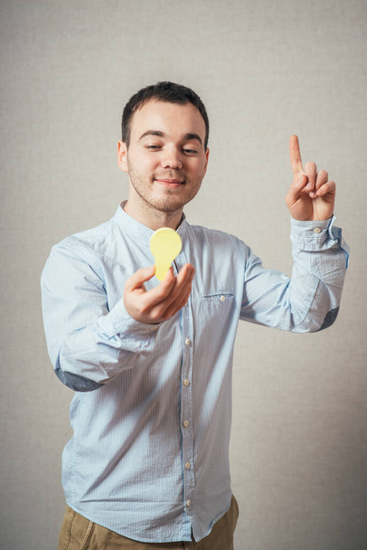 man close-up on a gray background holding a light bulb sticker - Foto, imagen