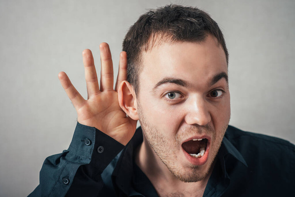 Man shows not hears, hand near ear. On a gray background. - Фото, изображение