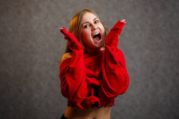 Girl tries on a red sweater on a gray background - Photo, Image